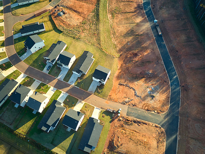 Aerial view of new housing development with completed homes alongside cleared lots and freshly paved roads prepared for future construction.